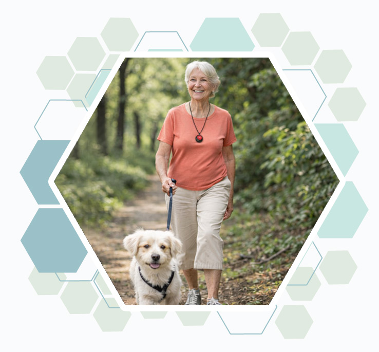 dame senior en promenade avec son chien en forêt et portant un pendentif de téléassistance détecteur de chute.